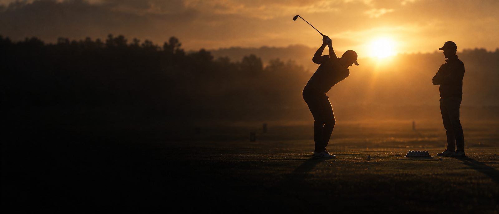 A coach watching a player hit balls at sunrise